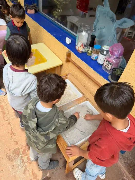 Niños de After School de espaldas, explorando juntos una mesa de agua junto a la ventana del salón