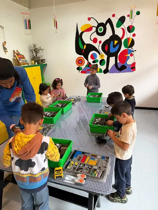 Niños de After School trabajando con cajas de material en el salón, frente a un mural de colores