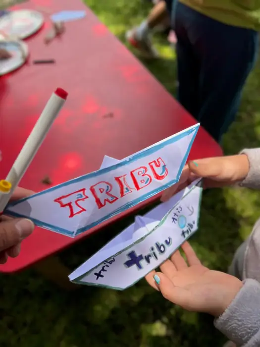 Niños de Camps sosteniendo barquitos y banderines de papel con el logo de Tribu, hechos a mano