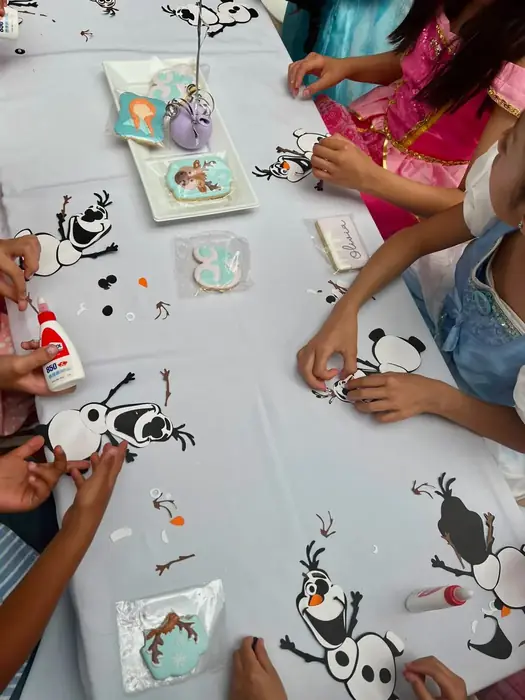 Niñas decorando galletas con figuras de Olaf sobre un mantel blanco, en una fiesta temática de Frozen