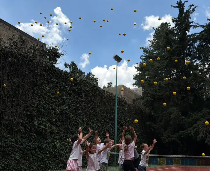 Niños de Fun Day a contraluz lanzando decenas de pelotas al cielo, en la cancha