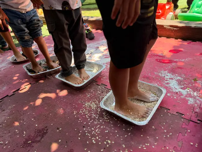 Pies descalzos de niños pisando charolas con pintura de colores, en un Fun Day de Tribu