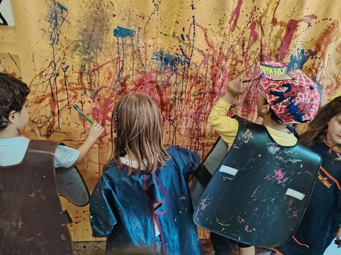 Niña de espaldas frente a una pared llena de salpicaduras de pintura, en un Fun Day de Tribu