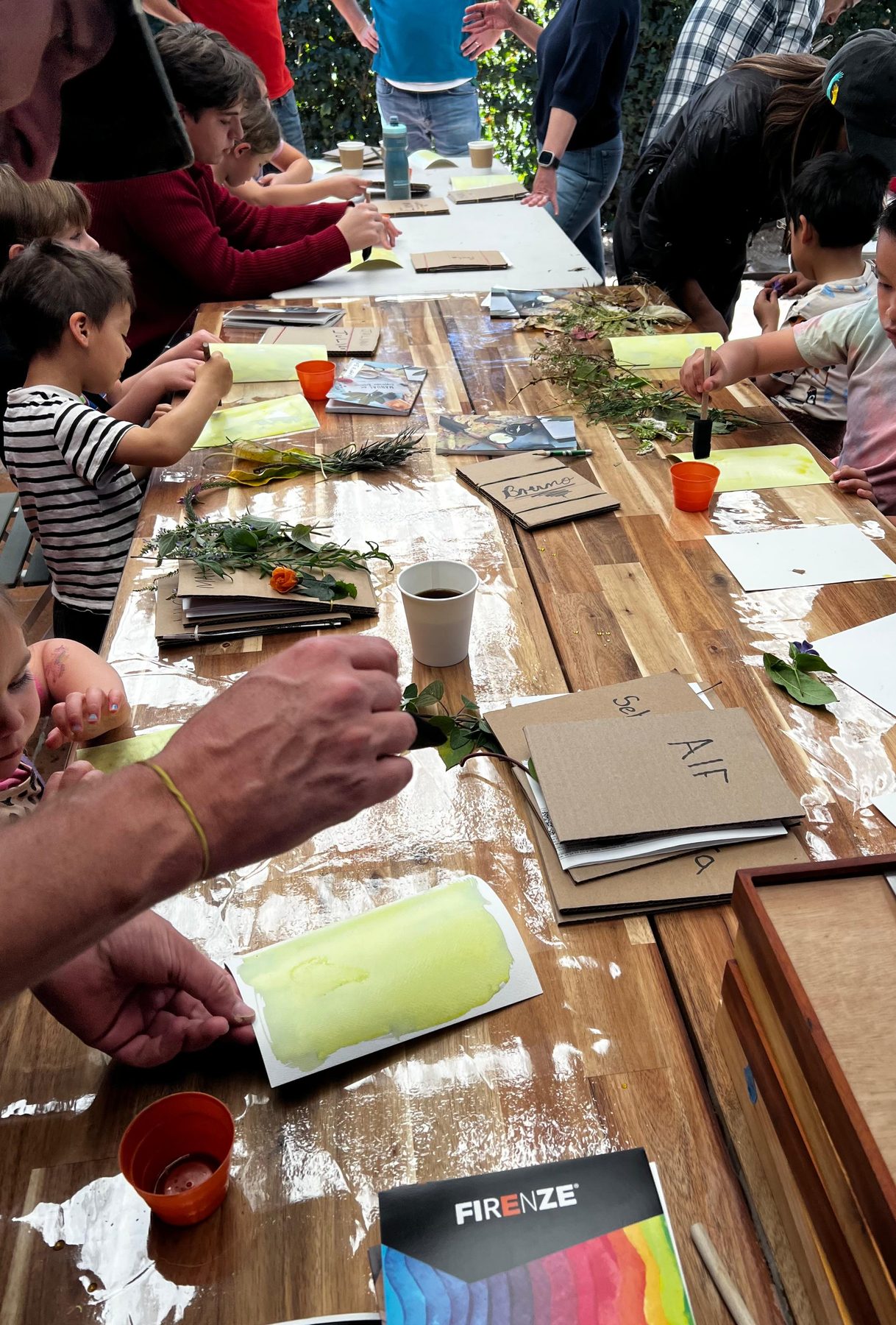 Mesa larga del taller con materiales y manos trabajando, en una Experiencia de Tribu