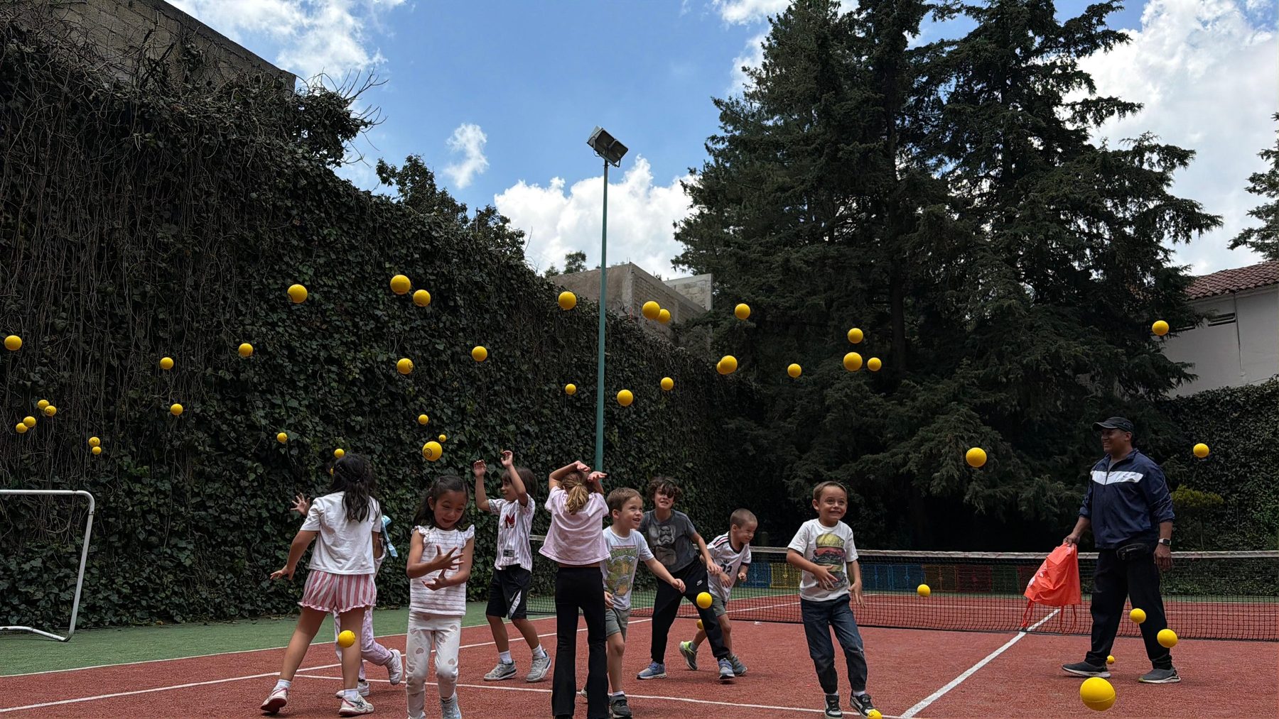 Cancha al aire libre con decenas de pelotas amarillas en el aire y niños jugando a lo lejos, en un Fun Day de Tribu